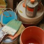 a bucket of paint next to a bucket of brushes