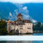 a castle sitting on top of a lake surrounded by mountains